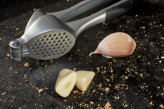 Garlic Crusher With Garlics And Scattered Bread Crumbs In A Black Background