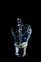 Creative broken light bulb with art water fountain on isolated black background with flash. The...