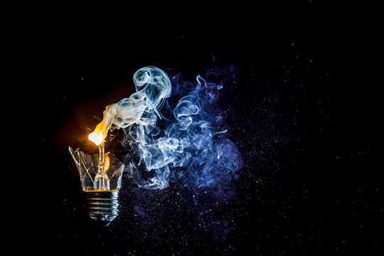 Сosmic explosion of burning light bulb with flying splinters of broken glass and smoke on isolate black background. Сoncept of creative art of starry sky, cosmos,  universe and the big bang theory.