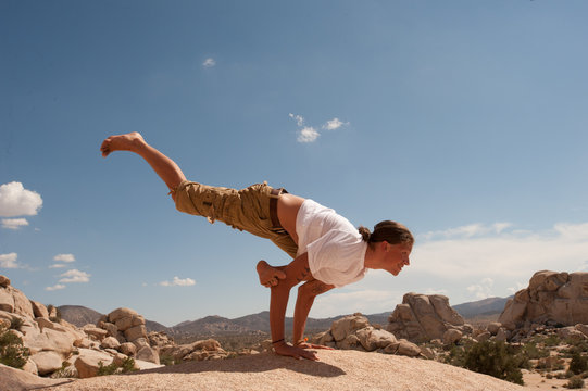 Young Man Playng With Extreme Yoga Pose In The Desert. A Version Of  EKA PADA KOUNDINYASANA (?)