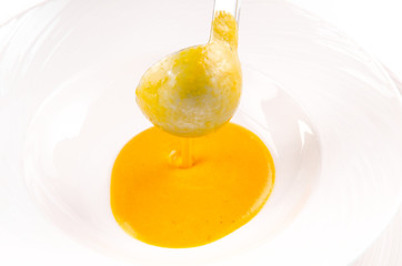 The chef pours a soup ladle pumpkin soup in a white plate