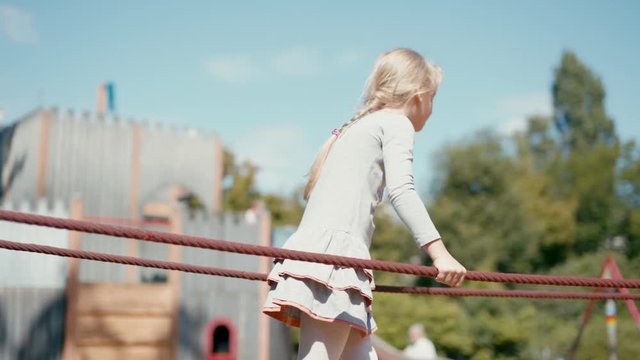 7 year old Cute Blond Girl is Playing on Playground and Walking on Rope Outdoors in Summer
