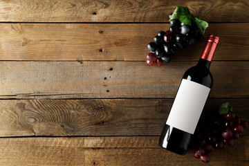 Red wine bottle with grapes on brown rustic wooden table flat lay from above