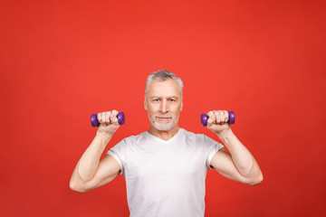 Fototapeta na wymiar Portrait Of A Senior Man Exercising with dumbbells against red Background.