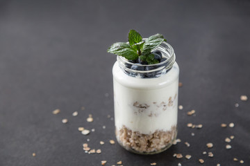 goblet of yogurt with cereals and fruits strewed on leaves mint