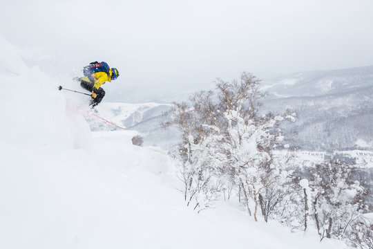 Man in yellow jumps off a cornice near the summit of a small peak in the backcountry of Hokkaido, Japan.