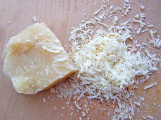 piece of Parmesan cheese on a wooden board and grated cheese. сlose up