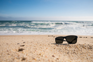 Sunglasses on beach, sunny summer day. Copy space on left.