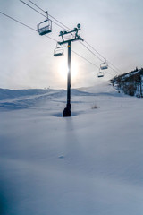 Fototapeta na wymiar Bright sky over ski lifts and snowy mountain