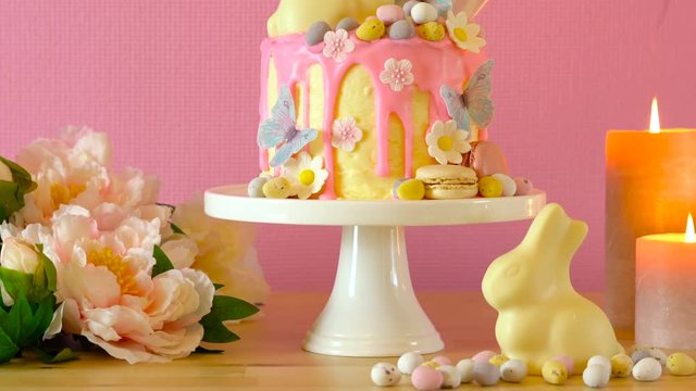 On-trend Easter theme candy land drip cake decorated with lollipops, cand eggs and white chocolate bunny in party table setting.