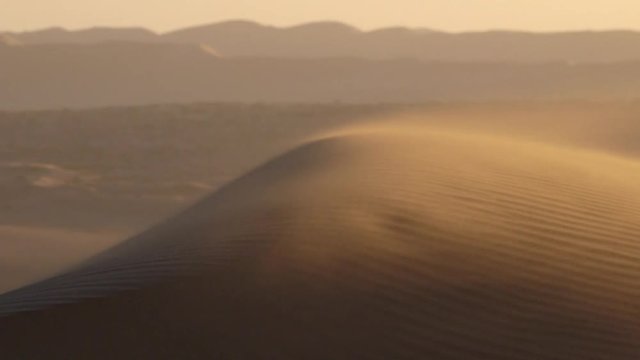 Wind blows swirling sand in dunes in vast empty Namib Desert landscape at sunset