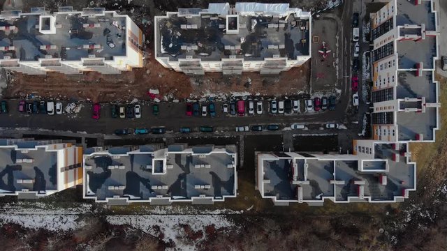 Aerial view of different cars standing inside a new modern microdistrict and a view of the house under construction with a crane near the road with cars moving along it
