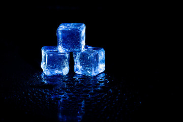 Blue ice cubes reflection on black table background.