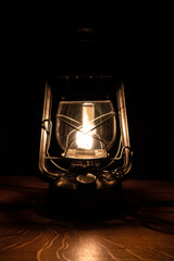 Fototapeta na wymiar old vintage oil lamp Lantern shining in darkness on handmade wooden table 