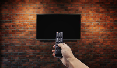Television on brick wall with hand using remote control