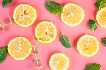 Fototapeta na wymiar Yellow lemon slices with mint leaves on pink background
