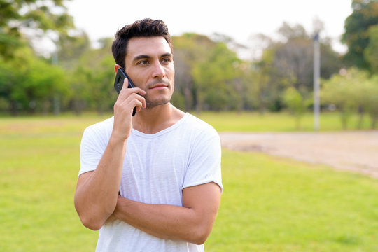 Young Handsome Hispanic Man Thinking And Talking On The Phone At Park