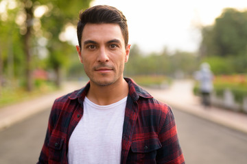 Face of young handsome Hispanic hipster man at the park