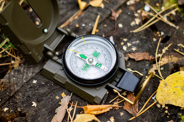 Compass on the ground with leaves and grass. Navigation and survival in the wild. Camping in nature.