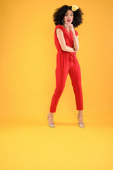 Fototapeta na wymiar Young African American Woman in Red Jumpsuit on Yellow Background