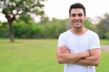 Happy young Hispanic man smiling with arms crossed in the park outdoors