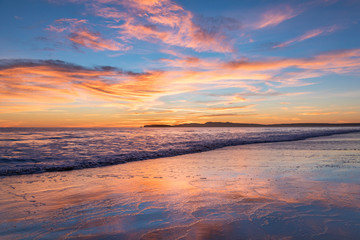 Fototapeta na wymiar Sunset at Limantour Beach, Pt. Reyes California. Facing northwest with saturated colors and reflections in the water.