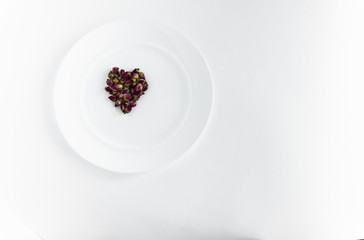 Small buds of red roses in the shape of a heart on a white plate