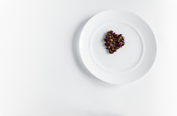 Small buds of red roses in the shape of a heart on a white plate