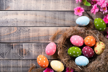 Happy easter! Colourful of Easter eggs in nest with pink flower and Feather on wooden background.