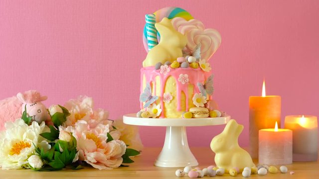 On-trend Easter theme candy land drip cake decorated with lollipops, cand eggs and white chocolate bunny in party table setting.
