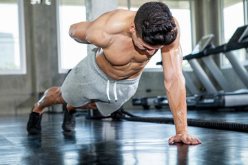 Fototapeta premium Muscular bodybuilder man doing push ups exercise with one hand in fitness gym . Shirtless young sport man training .work out healthy