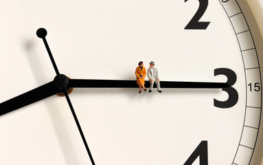 A miniature old couple sitting on a clock's needle. - obrazy, fototapety, plakaty