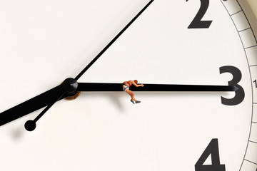A miniature woman hanging from a clock needle.