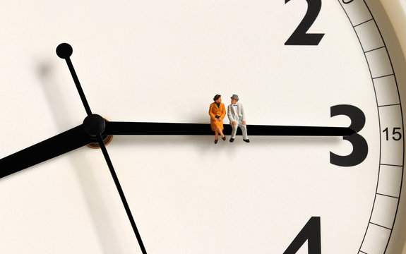 A miniature old couple sitting on a clock's needle.