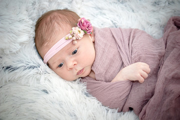 Female infant wrapped in mauve with pink flower headband facial closeup with open eyes