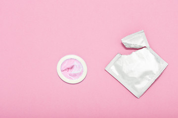 Opened condom and condom in pack on a pink background. A condom use to reduce the probability of...