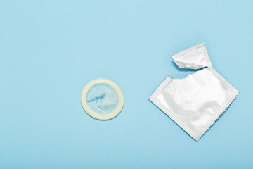 Opened condom and condom in pack on a blue background. A condom use to reduce the probability of...