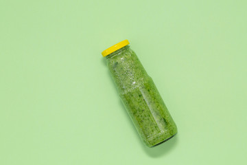 Colorful green smoothie in bottle on green background, top view. Healthy food for breakfast and snack.