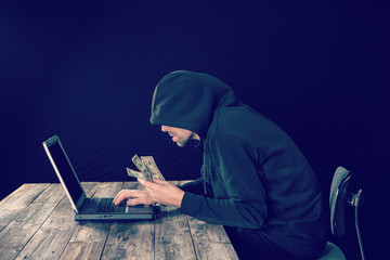 hacker in black hoody with laptop and dollar notes