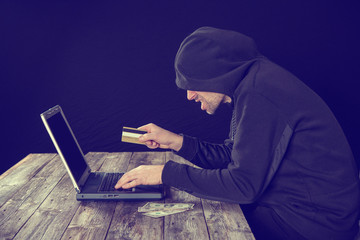 hacker in black hoody with laptop, bank card and dollar notes