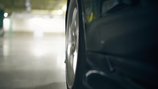 wonderful close view black car wheel drives on gray asphalt on underground parking lot reflecting light
