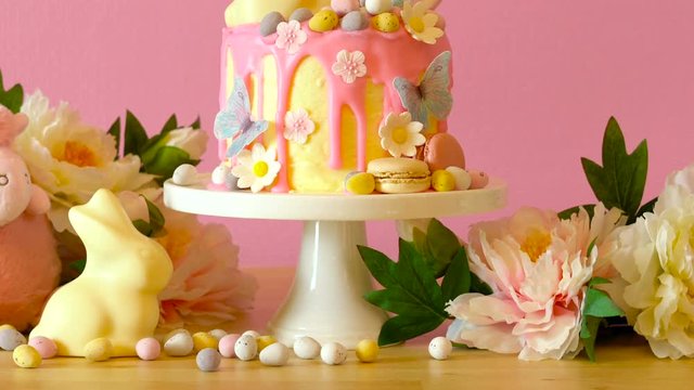 On-trend Easter theme candy land drip cake decorated with lollipops, cand eggs and white chocolate bunny in party table setting.