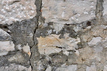 Background ancient old grey and white stone wall with a vertical crack, fissure and grey cement mortar.