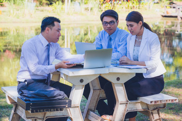 Business team work. They  are sitting on bench and talking in the park.  they are talking about business and  on table had a notebook and a glass of coffee.Photo concept  business and team work.