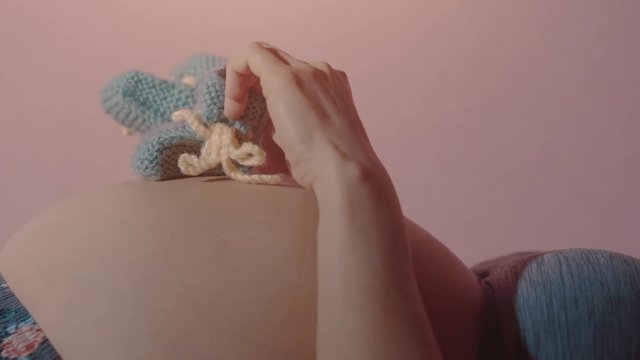 Pregnant woman lying on her back and stepping with blue baby shoes on her naked pregnant belly