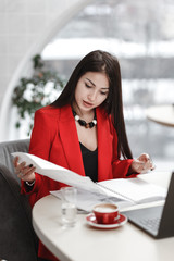 Stylish young woman designer is working at the design project of interior sitting at the desk with laptop and documentation