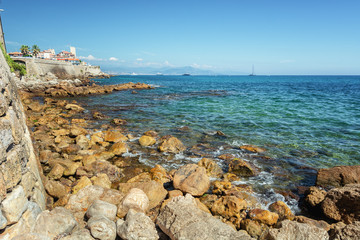 The old city wall along the coast of the French town of Antibes with the old old center in the...