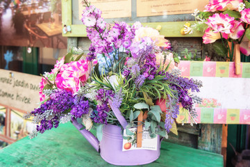 Table decorated with a purple watering can filled with artificial flowers in all kinds of shades of purple.
