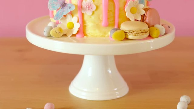 On-trend Easter theme candy land drip cake decorated with lollipops, cand eggs and white chocolate bunny in party table setting.