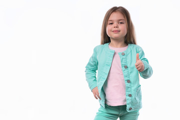 Obraz na płótnie Canvas Portrair of beautiful little girl showing thumbs up or Like sign. The portrait is made on a white background. Girl looks into the camera artistically.
